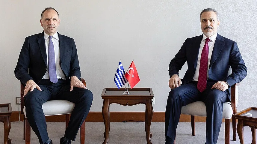 Dva muškarca u odijelima sjede na stolicama, sa zastavama Grčke i Turske između njih.