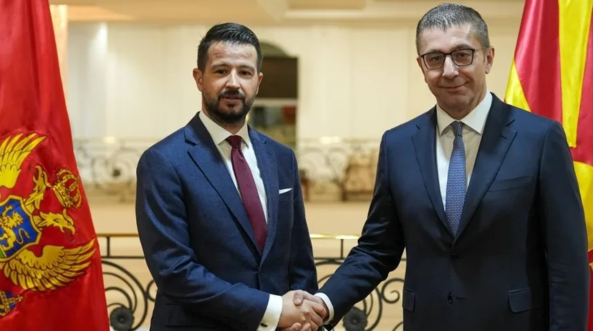 Dvojica političara, jedan iz Crne Gore i drugi iz Sjeverne Makedonije, rukuju se ispred zastava svojih država.