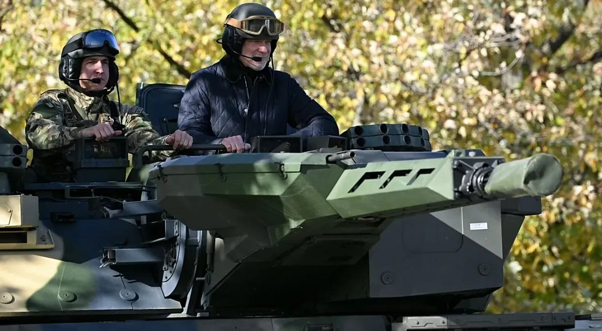 Dva vojnika u tenku, jedan u uniformi, drugi u jakni, nose kacige i naočale.