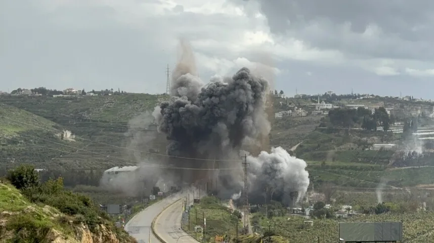 Velika crna i siva dimna eksplozija iznad naseljenog područja sa zelenim brdima u pozadini.