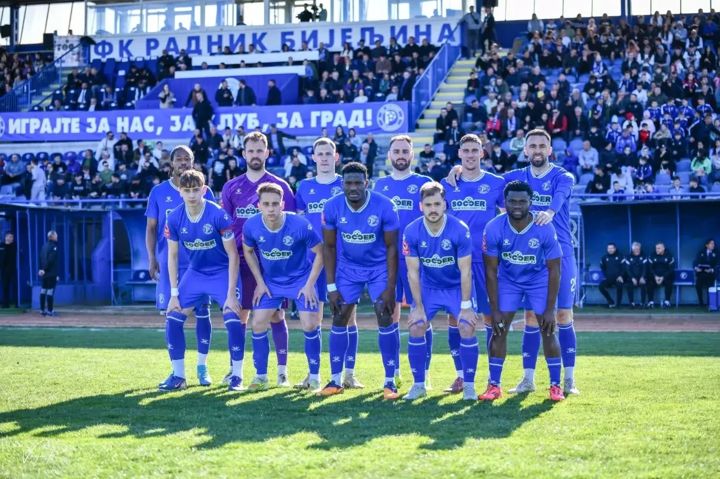 Fudbalski tim FK Radnik Bijeljina pozira na terenu pred utakmicu, nose plave dresove.