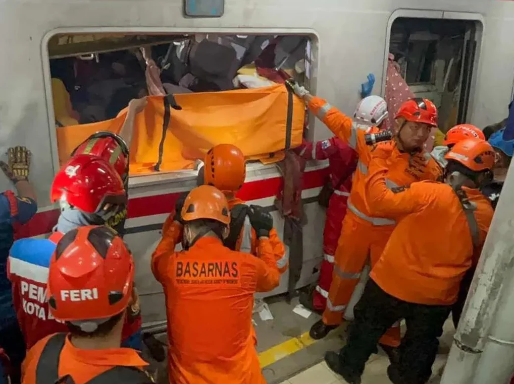 Vatrogasci i spasioci u narandžastim uniformama izvlače tijelo umotano u narandžastu vreću iz smrskanog voza.