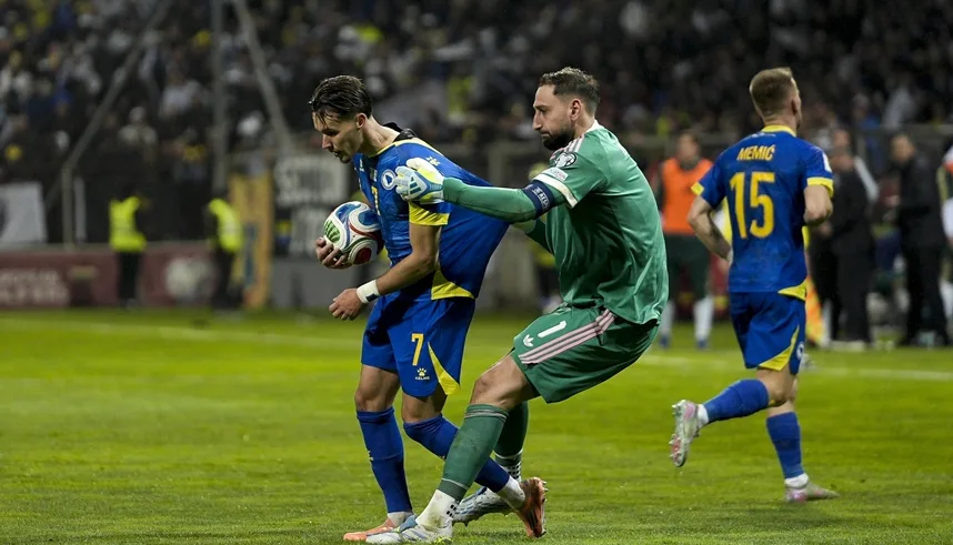 Fudbaler u plavom dresu sa brojem 7, drži loptu, dok mu golman u zelenom dresu pokušava oduzeti posjed.