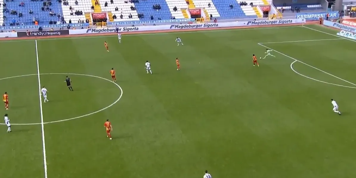 Fudbaleri u bijelim i crveno-žutim dresovima na zelenom fudbalskom terenu tokom utakmice.