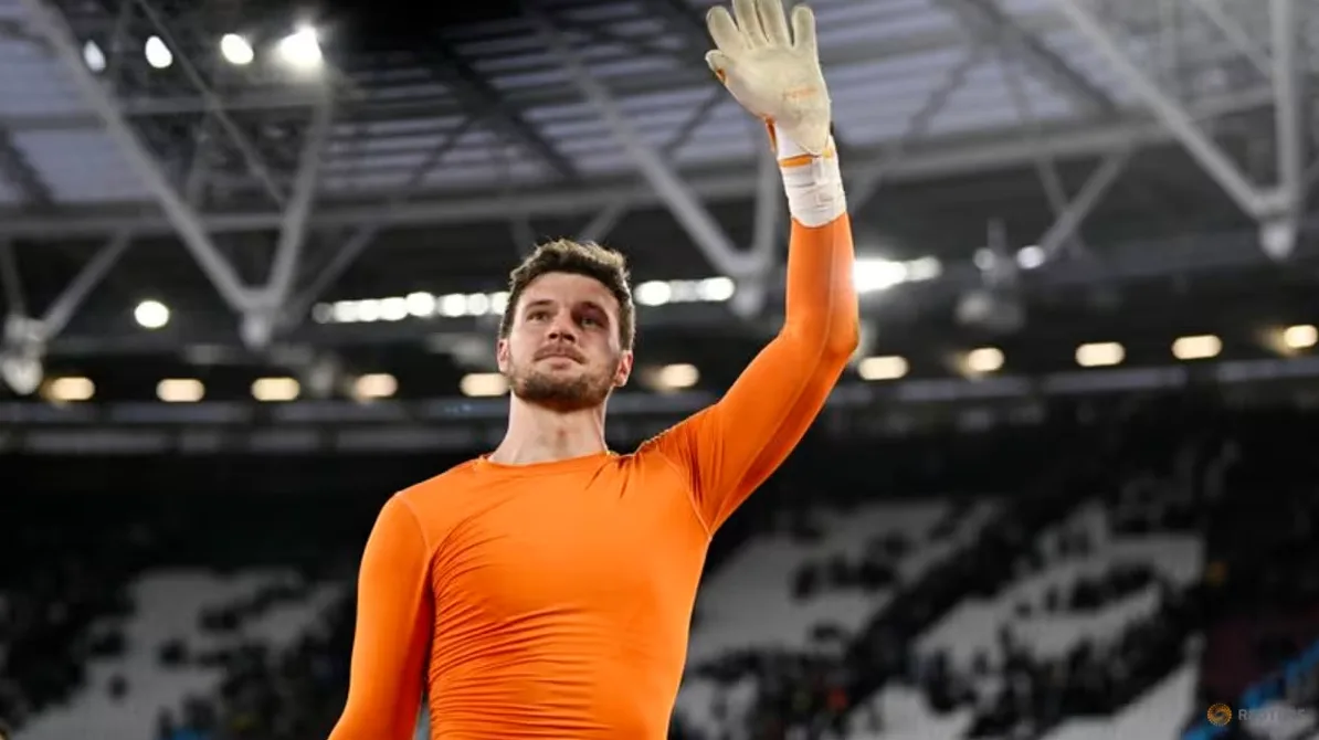 Fudbalski golman u narandžastom dresu podiže ruku u pozdrav