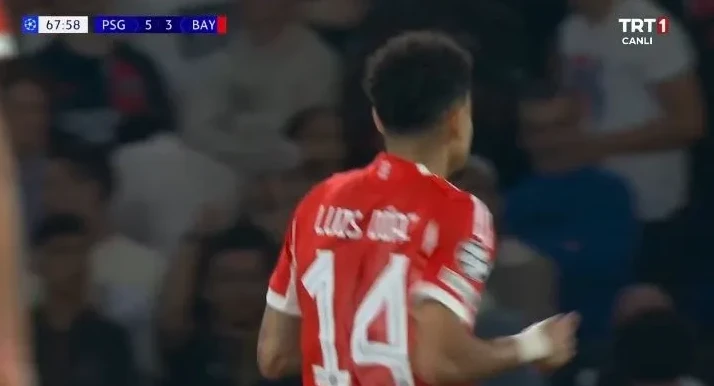 Fudbaler u crvenom dresu sa brojem 14 na leđima, vjerovatno iz tima Bayerna, na fudbalskoj utakmici. U gornjem lijevom uglu vidljiv je rezultat PSG 5 - 3 BAY.