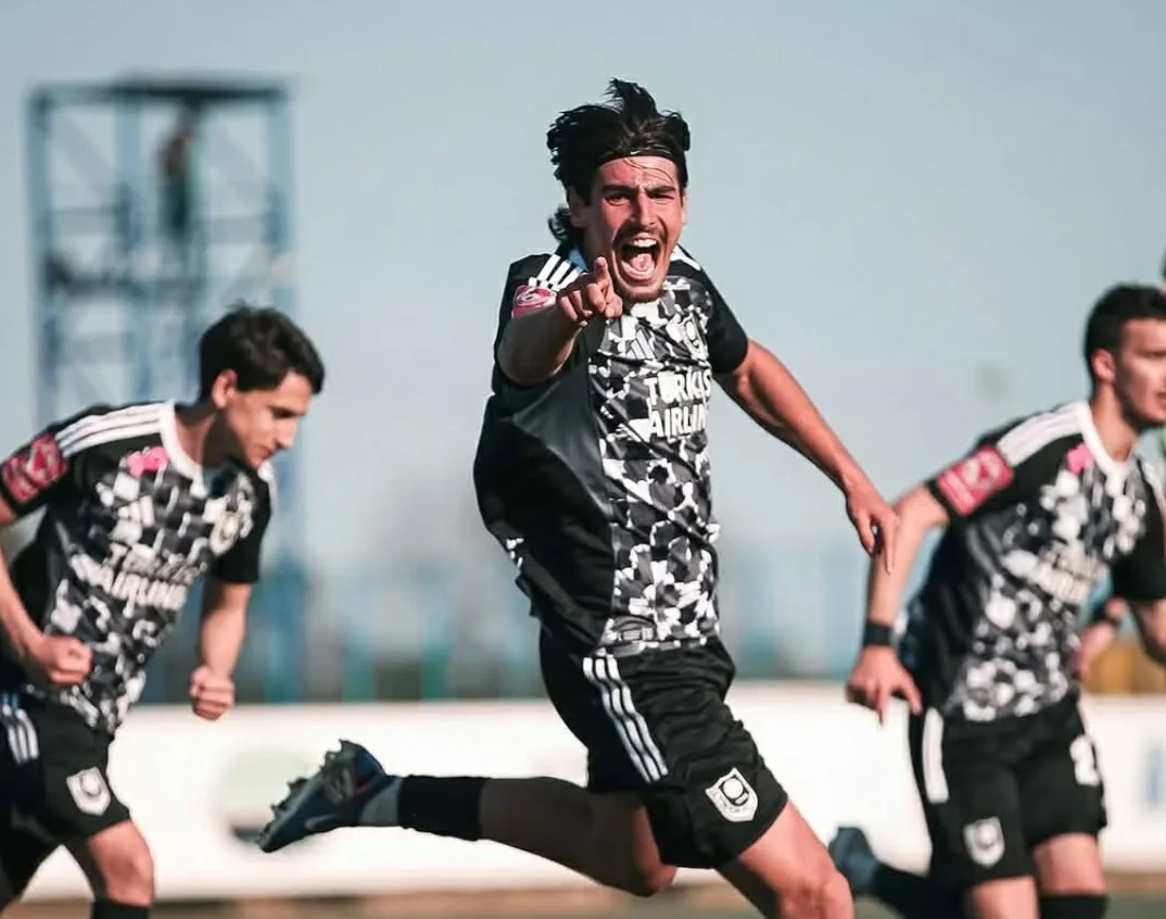 Fudbaler u crno-bijelom dresu sa maskirnim dezenom slavi postignut gol, pokazujući prstom ka kameri.