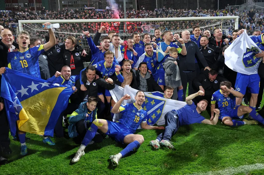Fudbalska reprezentacija Bosne i Hercegovine proslavlja pobjedu na stadionu, ogrnuti državnom zastavom.