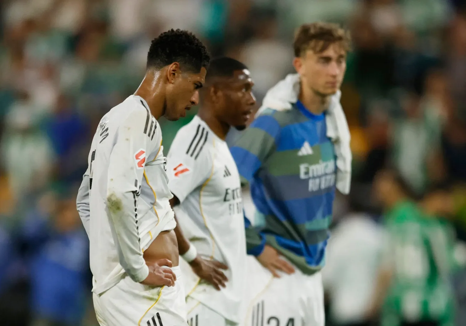 Tri fudbalera Real Madrida stoje na terenu nakon utakmice, gledajući u daljinu sa razočaranim izrazima lica.