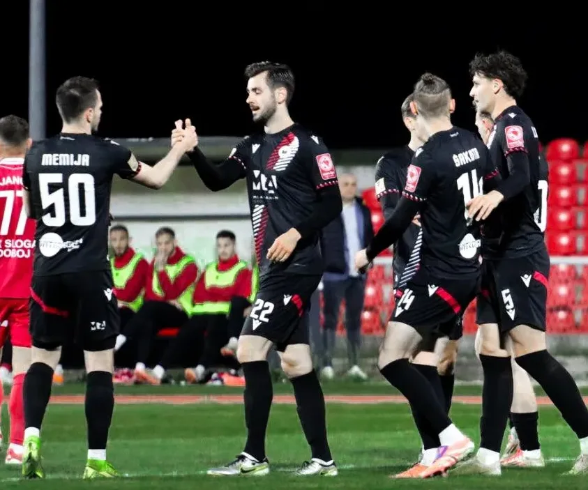 Dva fudbalera crno-bijelih dresova se rukuju na terenu