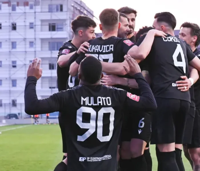 Grupa fudbalera u crnim dresovima zagrljena slave gol ili pobjedu na terenu.