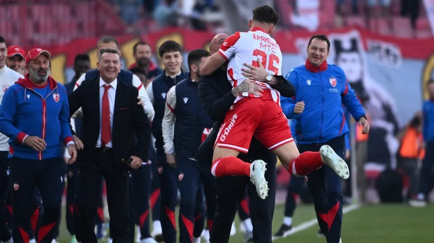 Fudbaleri u crveno-bijelim dresovima slave pobjedu, jedan igrača drži drugi u zagrljaju.