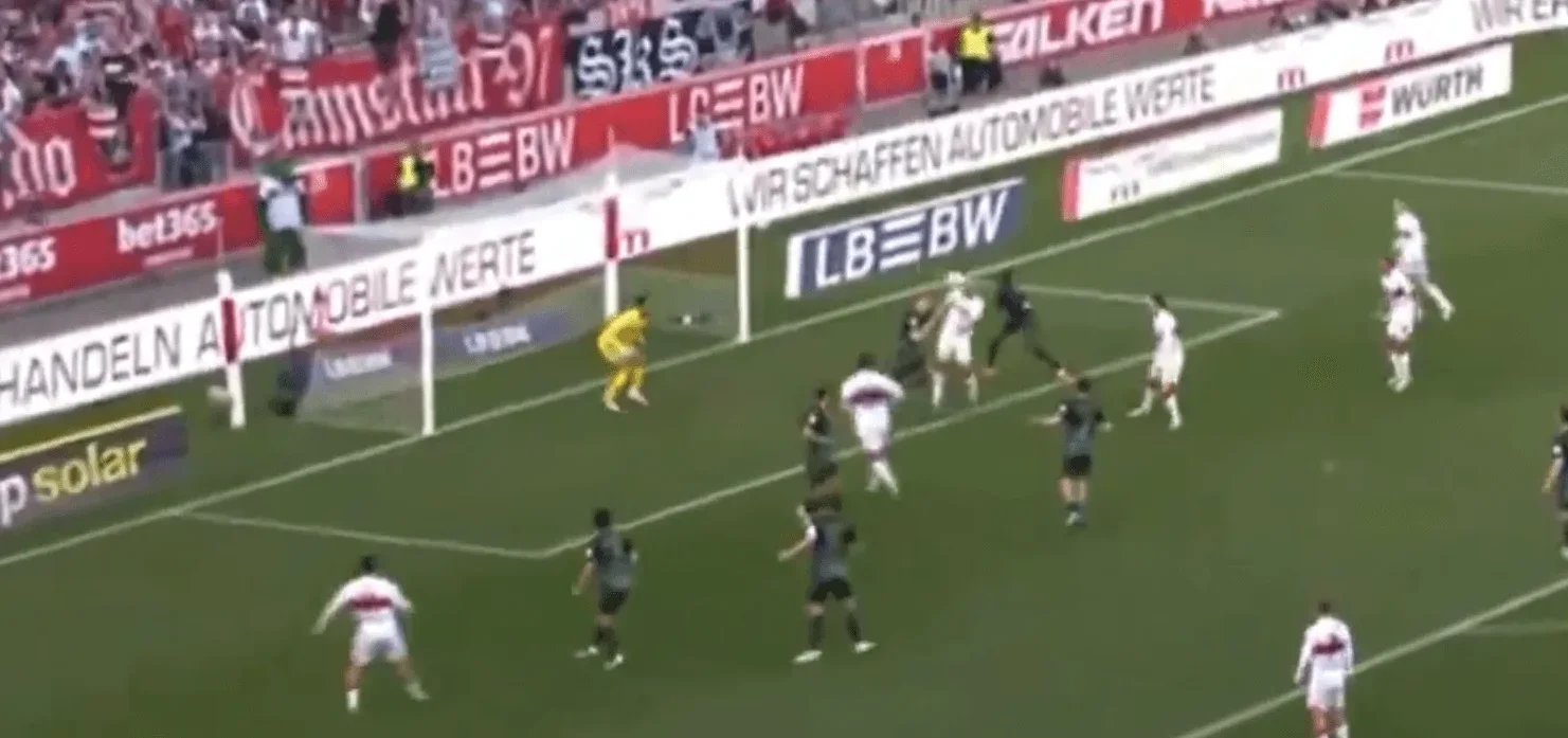 Fudbaleri u bijelim i crnim dresovima bore se za loptu na zelenom terenu ispred gola.