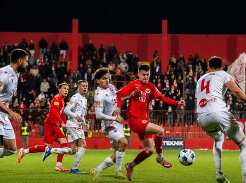 Fudbaleri u bijelim i crvenim dresovima na terenu tokom noćne utakmice.