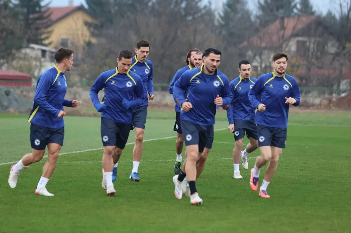 Fudbaleri u plavim dresovima trče na zelenom terenu tokom treninga.