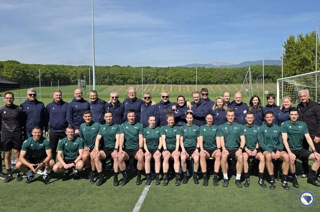 Grupa fudbalskih sudija iz Bosne i Hercegovine pozira za grupnu fotografiju na fudbalskom terenu.
