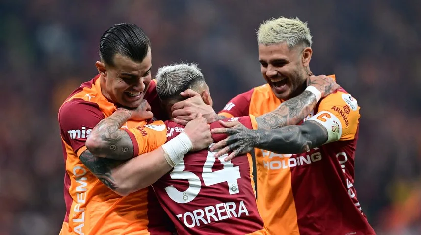 Troje fudbalera Galatasaraya slave pogodak, grleći se na terenu.