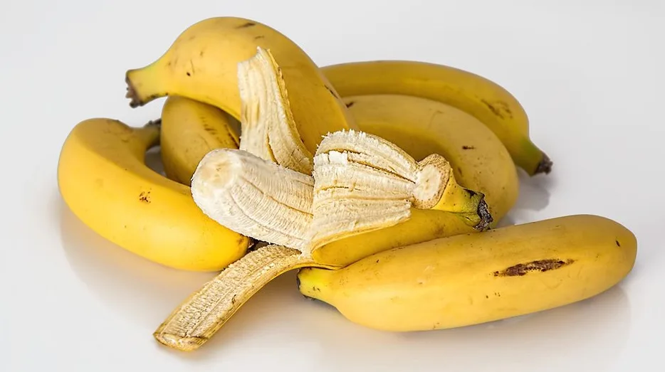 Grupa od nekoliko zrelih, žutih banana, od kojih je jedna djelimično oljuštena, prikazana na bijeloj podlozi.