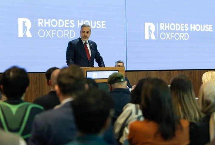 Predavač u odijelu drži govor ispred natpisa "Rhodes House Oxford"