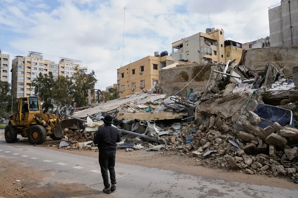 Građevinska mašina i čovjek stoje ispred srušene zgrade nakon sukoba ili katastrofe.