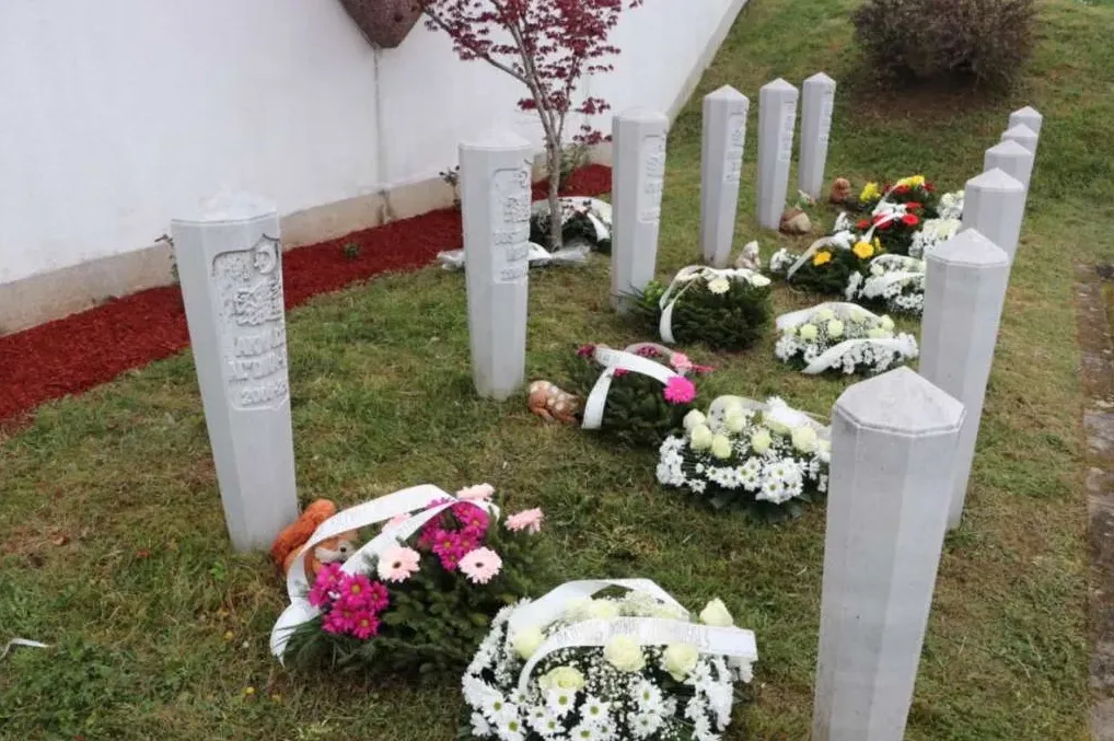 Redovi nadgrobnih spomenika sa cvjetnim aranžmanima i igračkama u groblju.