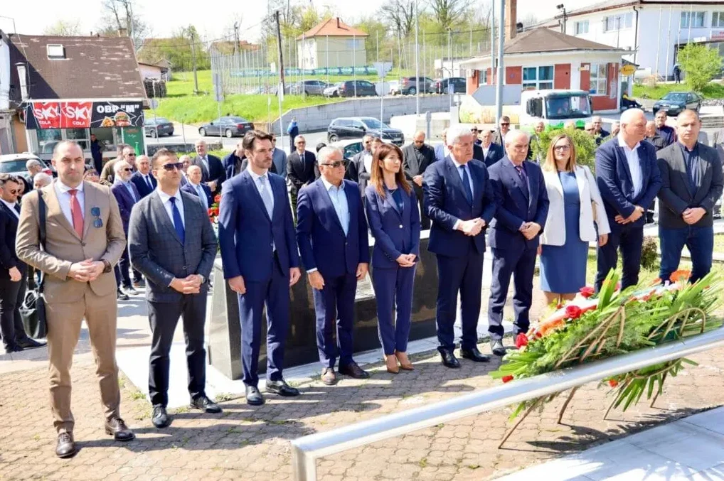 Grupa zvaničnika u odijelima stoji u počasnoj gardi pored vijenca položenog povodom obilježavanja značajnog događaja.
