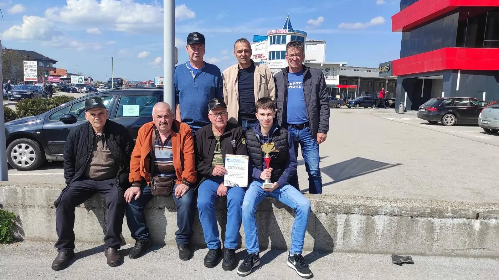 Grupa muškaraca pozira sa diplomom i peharom, jedna osoba drži pehar i diplomu.