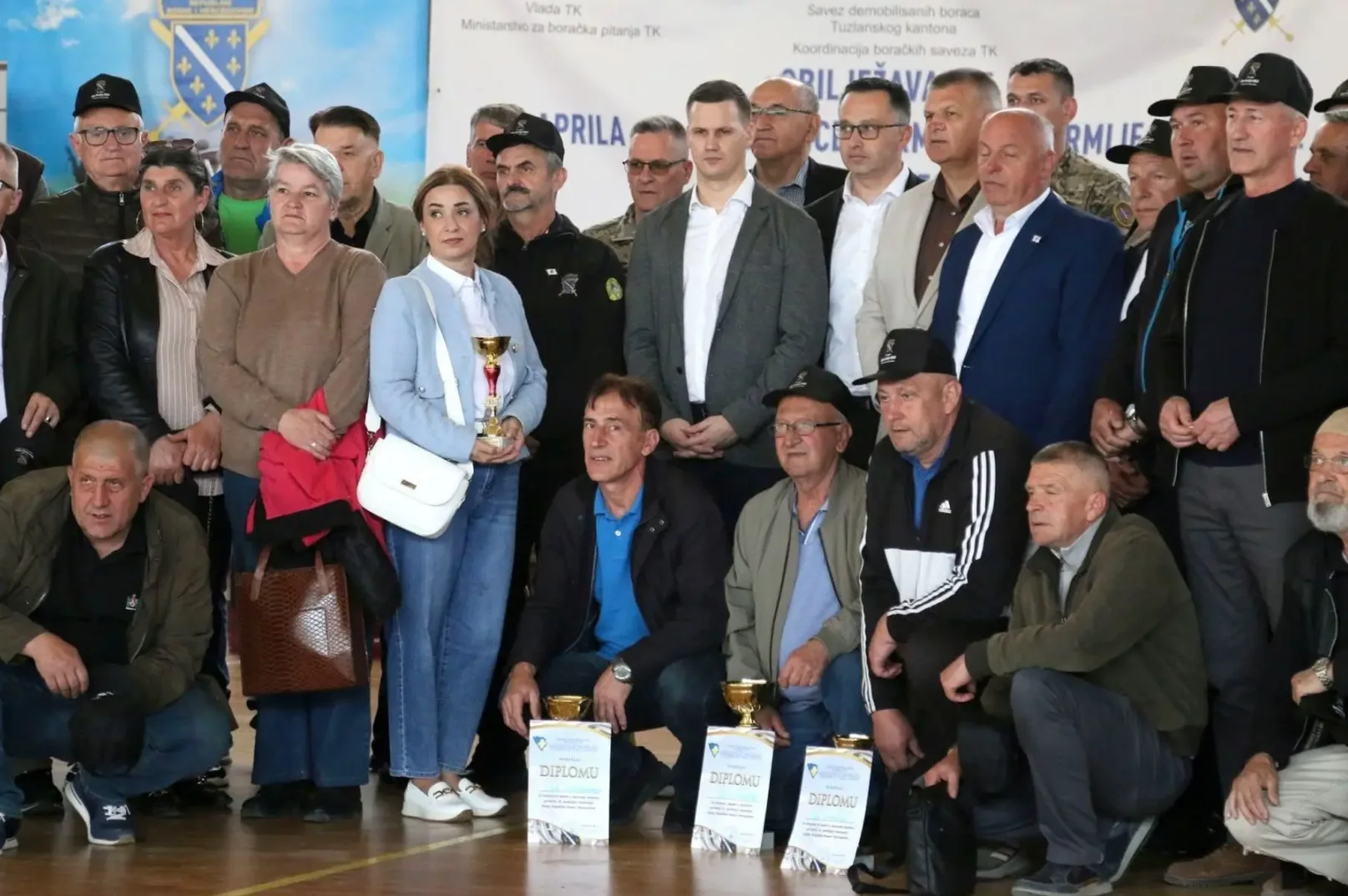 Grupa muškaraca i žena pozira pred kamerom sa peharima i diplomama u rukama i na podu.