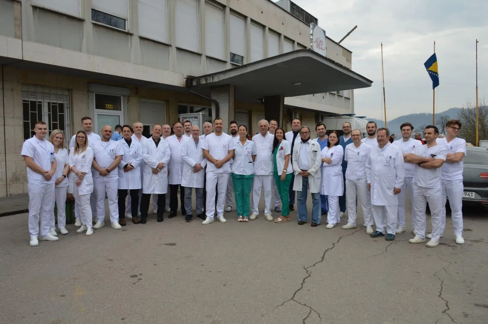 Grupa medicinskih radnika u bijelim uniformama ispred zgrade bolnice