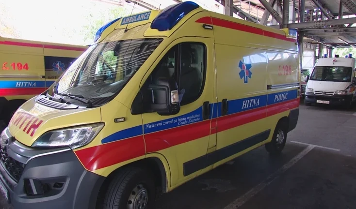 Žuta ambulantna kola hitne pomoći sa plavim i crvenim prugama i oznakom "HITNA POMOĆ" i "AMBULANCE".
