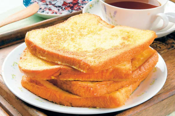 Hrskavi francuski hleb poslužen na tanjiru sa džemom i šoljom čaja u pozadini.