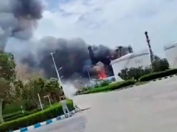 Veliki crni dim suklja iz industrijskog postrojenja u plamenu.