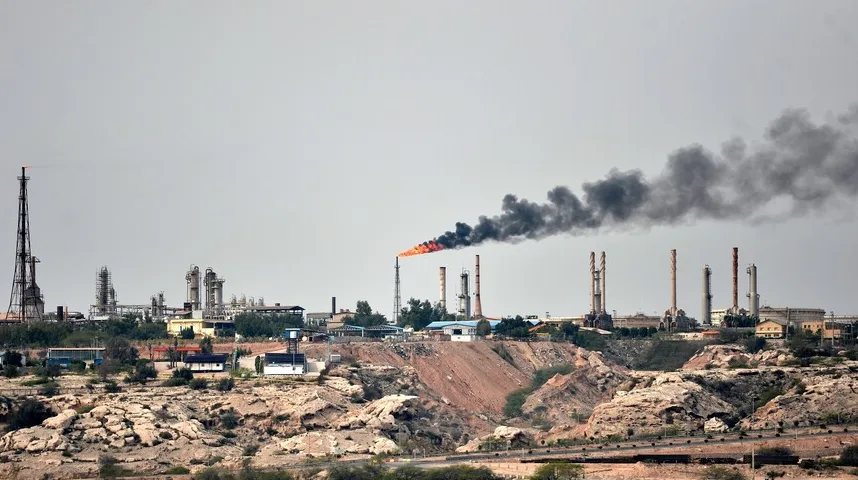 Industrijsko postrojenje sa velikom bakljom i tamnim dimom koji izlazi iz dimnjaka.