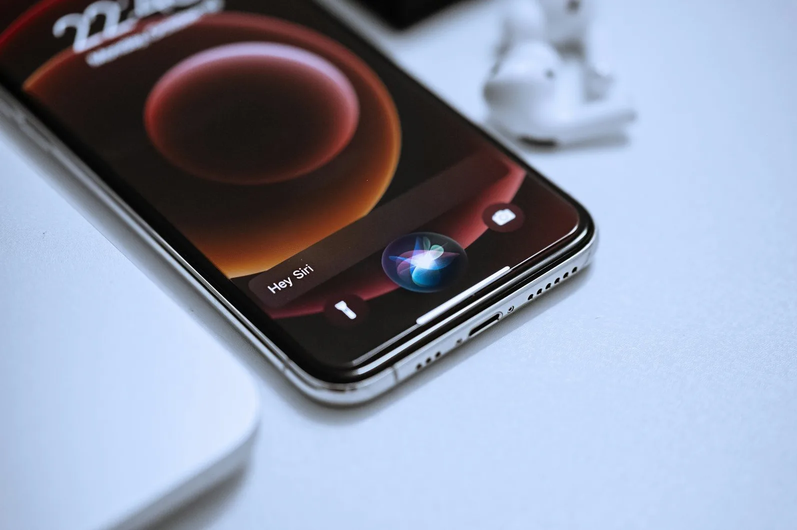 iPhone sa uključenim Siri asistentom i bežičnim slušalicama u pozadini.