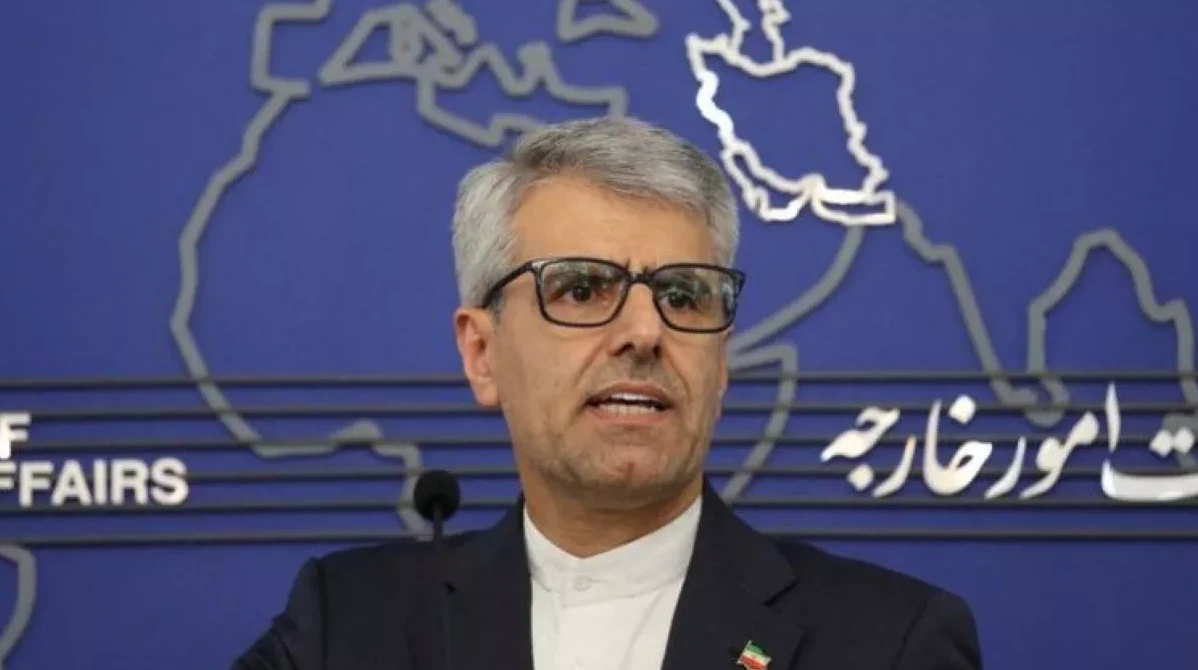 Portret iranskog ministra vanjskih poslova u odijelu i naočalama, s kartom svijeta u pozadini.