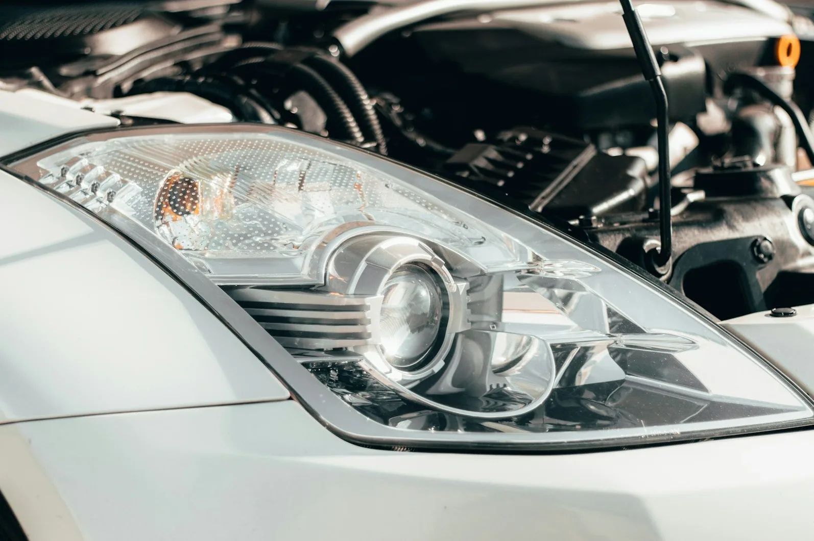 Detaljan pogled na prednji far bijelog automobila, sa vidljivim unutrašnjim dijelovima projektorske sijalice i detaljima na providnom kućištu.