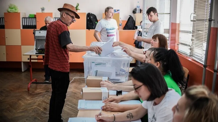 Stariji čovjek u šeširu ubacuje glasački listić u prozirnu kutiju.