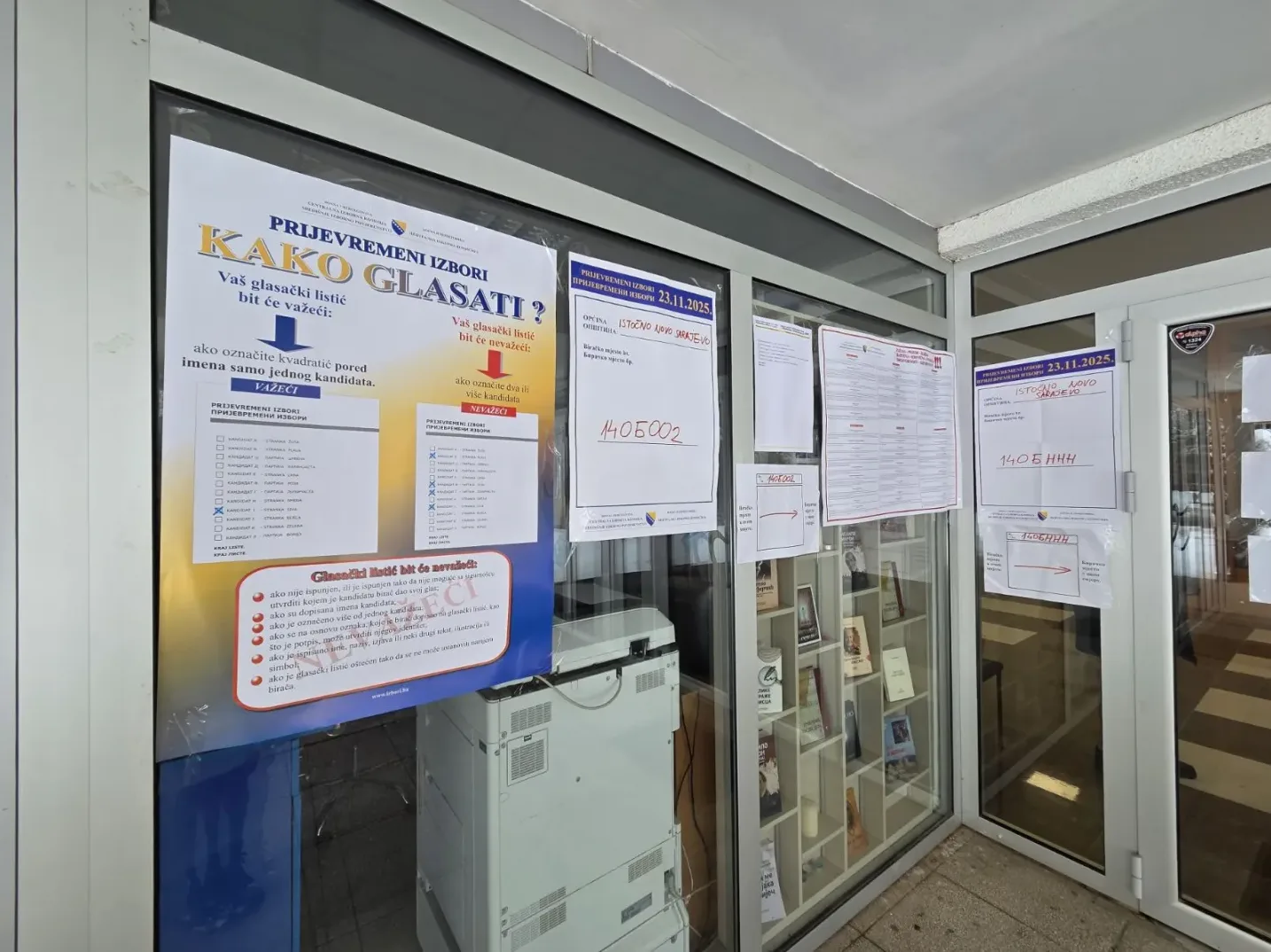 Plakat "Kako glasati?" postavljen na izlogu, sa uputama za glasanje na privremenim izborima. Vidljivi su datumi i nazivi općina.