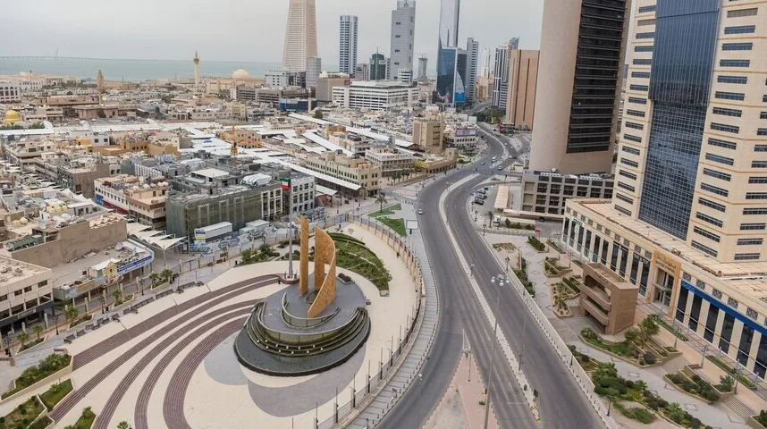 Aerialni pogled na prazan gradski trg s modernim spomenikom u centru, okružen višespratnim zgradama i praznim ulicama.