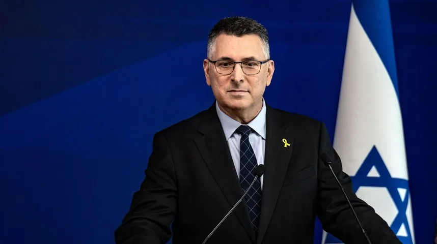 Portret izraelskog zvaničnika u crnom odijelu i plavoj kravati, sa žutom vrpcom na reveru. U pozadini je plava pozadina i zastava Izraela.