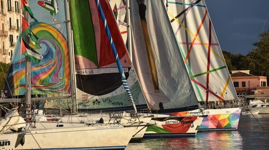 Višebojne jedrilice sa slikovitim jedrima usidrene u luci pri zalasku sunca.