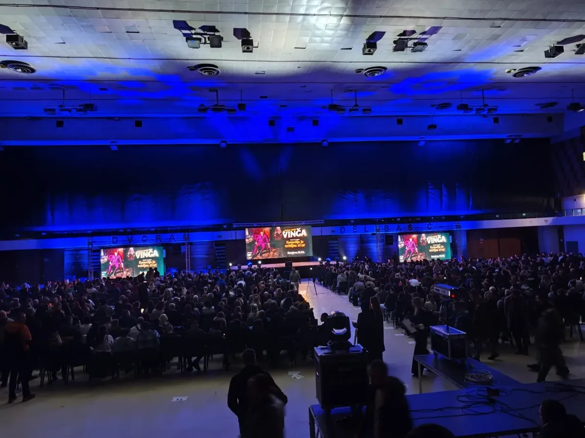 Velika sala ispunjena publikom, sa velikim LED ekranima na pozornici koji prikazuju logo i informacije o događaju