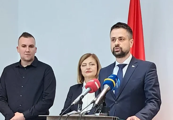 Tri osobe stoje iza postolja sa mikrofonima, sa zastavom Crne Gore u pozadini.