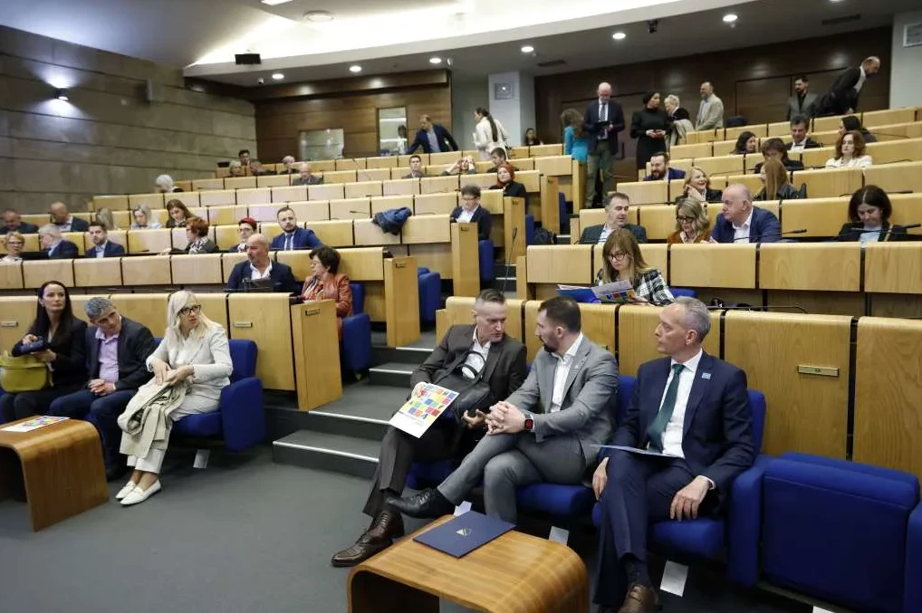 Grupa ljudi sjedi u moderno opremljenoj konferencijskoj sali.