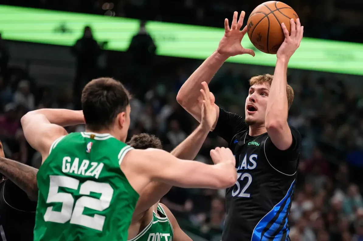 Košarkaš u crnom dresu s brojem 32 na leđima, kako podiže košarkašku loptu iznad glave, spremajući se za šut ili dodavanje.