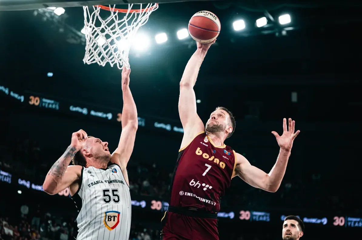 Košarkaši u akciji pored koša, jedan igrač pokušava zakucati loptu.