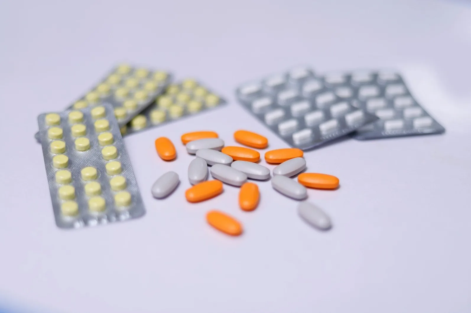 Blisteri sa žutim i bijelim tabletama, te rasute narandžaste i sive tablete na bijeloj podlozi.