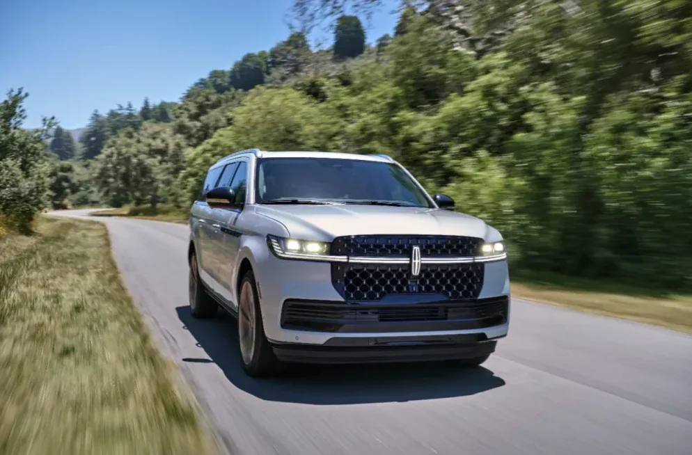 Srebrni Lincoln Navigator SUV koji se vozi zavojitom cestom okruženom zelenim drvećem i prirodom.