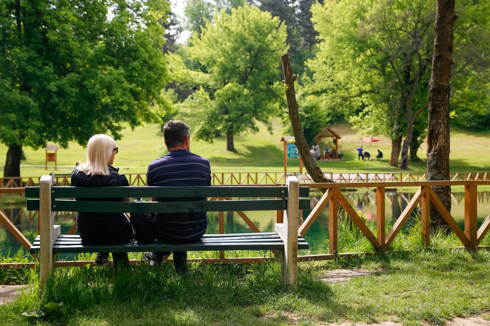 Par sjedi na klupi u parku i gleda prema jezeru.