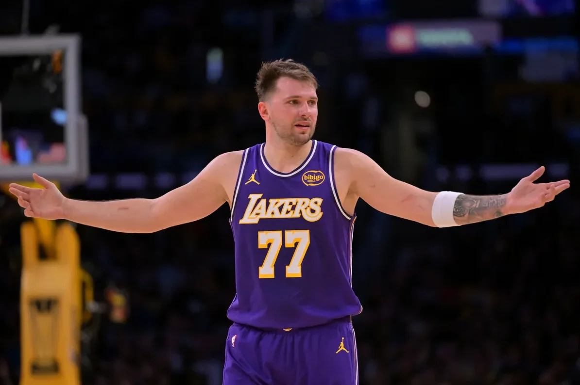 Luka Dončić u ljubičastom dresu Los Angeles Lakersa sa brojem 77 na leđima, raširenih ruku na košarkaškom terenu.